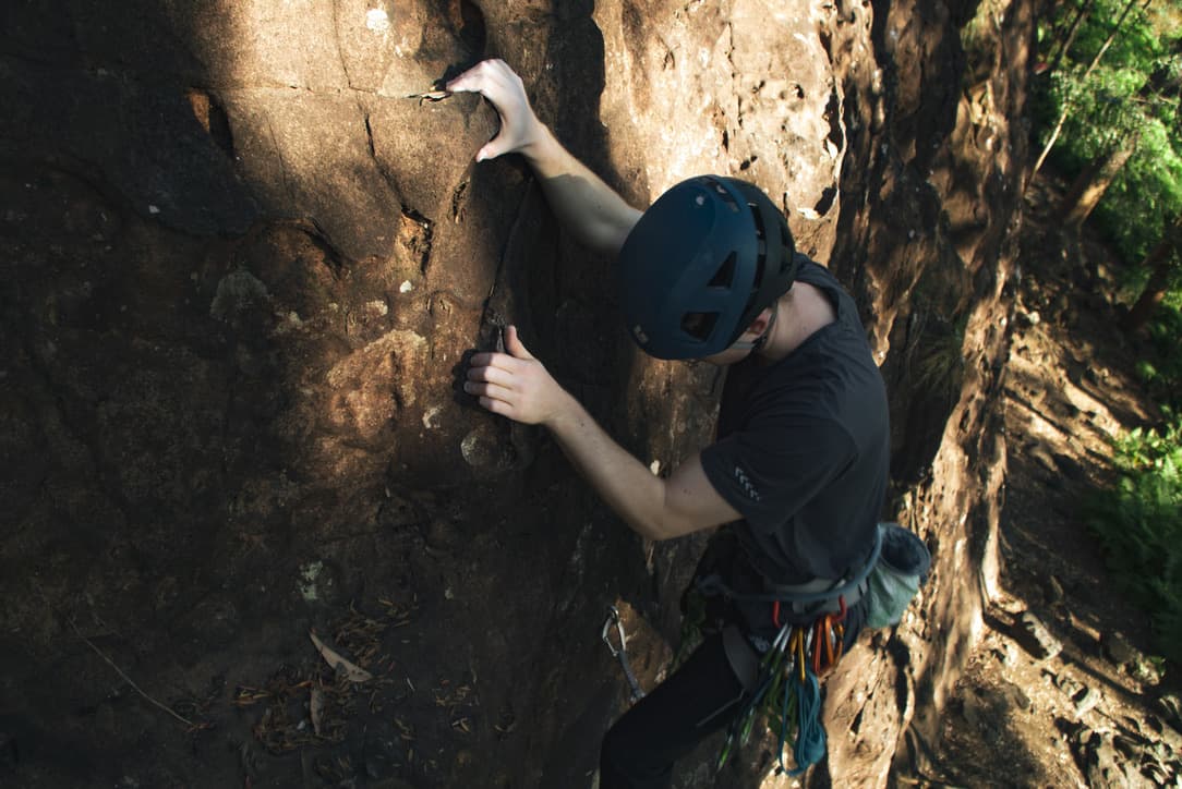 Bryce mid-route on an outdoor sandstone climb, a rack of gear on the harness